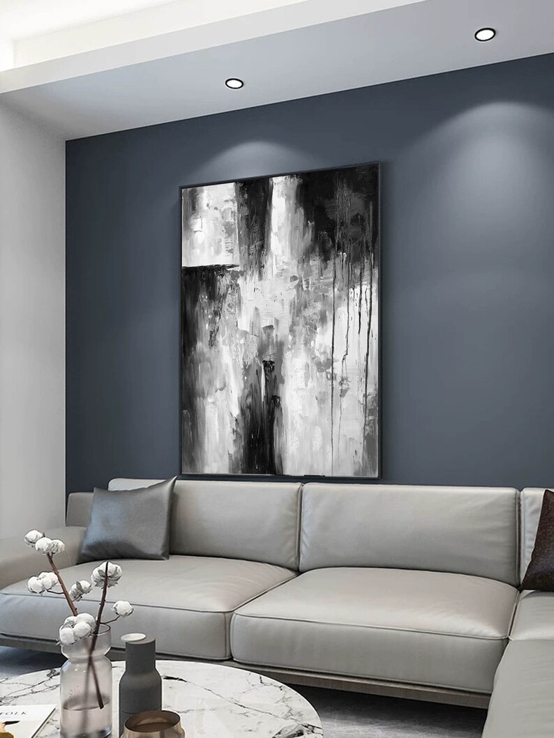 Puede incluir: Una pintura abstracta en blanco y negro con un sof&aacute; gris y una mesa de caf&eacute; de m&aacute;rmol en primer plano. La pintura est&aacute; colgada en una pared gris.
