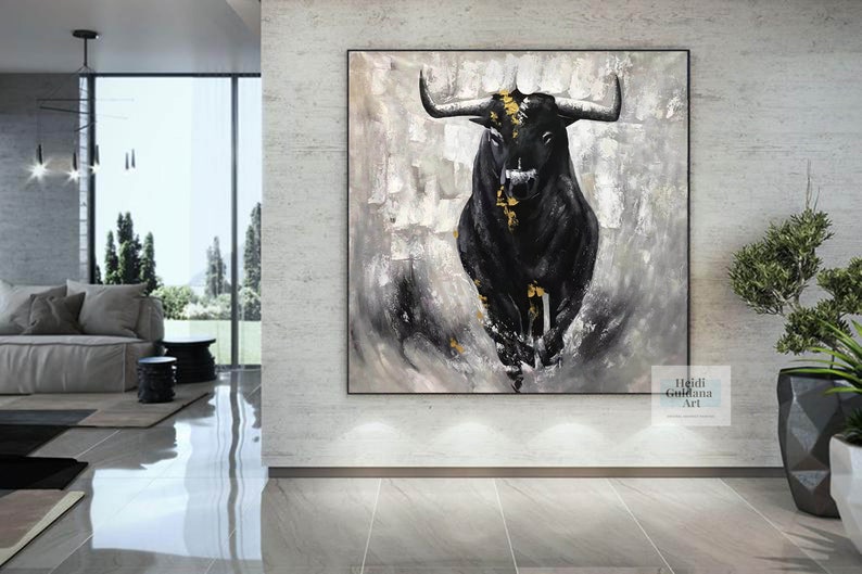 May include: Abstract black bull painting with gold accents on a textured gray and white background. The artwork is framed in black and hangs on a light gray wall. The painting is in a modern living room setting.