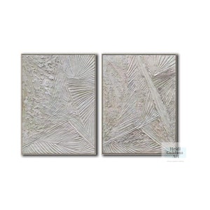 May include: A set of two abstract paintings with a textured, white and gray color scheme. The paintings are framed in a thin, silver frame.