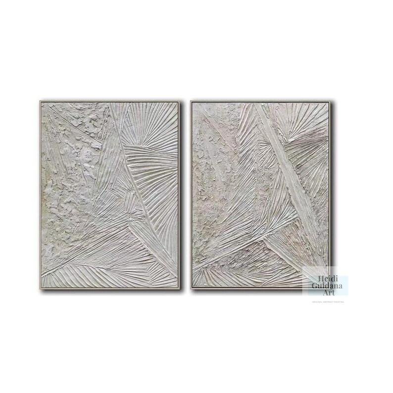 May include: A set of two abstract paintings with a textured, white and gray color scheme. The paintings are framed in a thin, silver frame.
