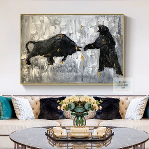 May include: A black and white abstract painting of a bull and a bear facing each other. The painting is on a canvas with a white background and gold accents. The painting is hanging on a wall above a couch with pillows and a coffee table.