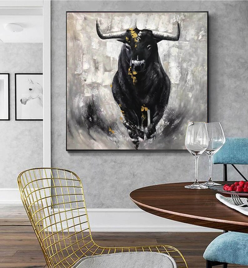 May include: A large, framed canvas art piece featuring a black bull with gold accents against a textured gray and white background. The bull is the focal point, with its horns and muscular form prominently displayed. The artwork is a modern, abstract representation.
