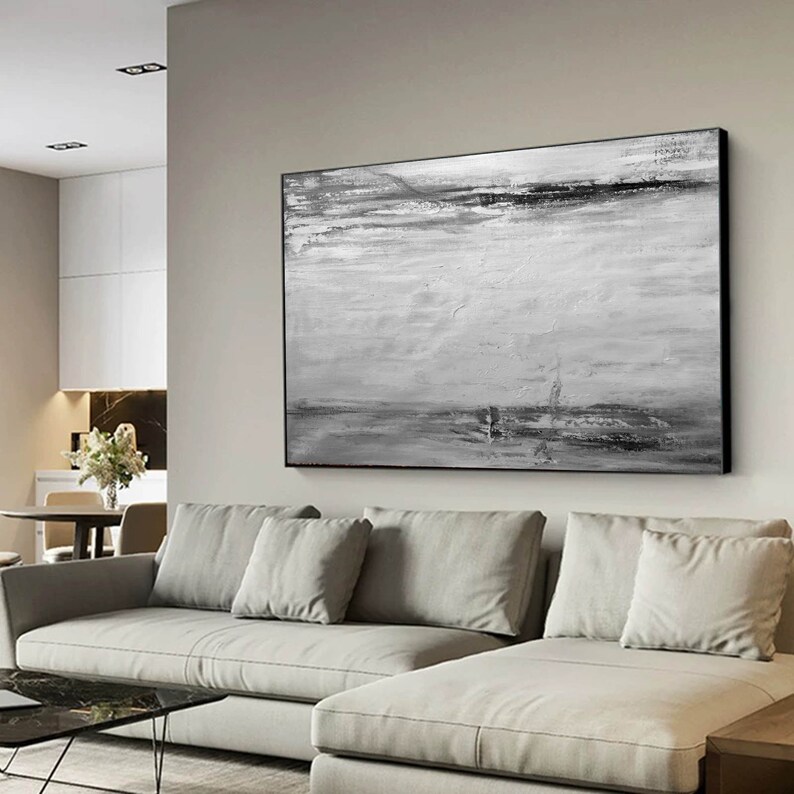 Op de afbeelding: Een zwart-wit abstract schilderij met horizontale penseelstreken. Het schilderij is ingelijst in een zwart frame en hangt aan een muur boven een witte bank.