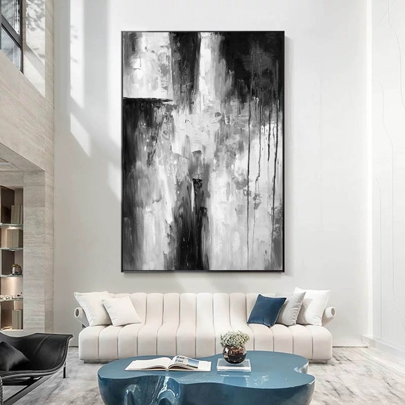Puede incluir: Pintura abstracta en blanco y negro con pinceladas gruesas y goteos de pintura. La pintura est&aacute; enmarcada y colgada en una pared blanca en una sala de estar moderna.