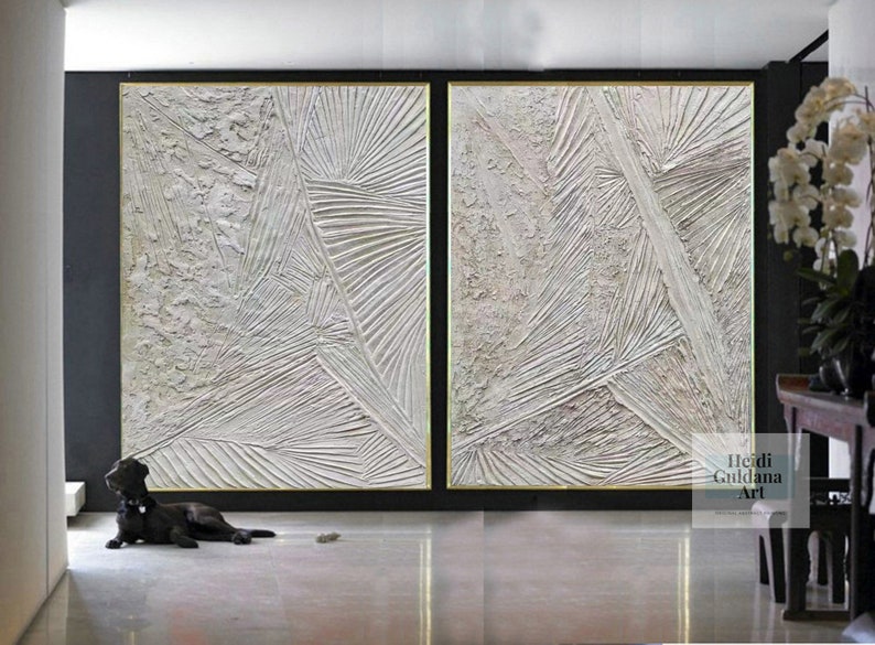 May include: Two large abstract paintings in white with textured lines and a gold frame. The paintings are hanging on a black wall in a modern interior.