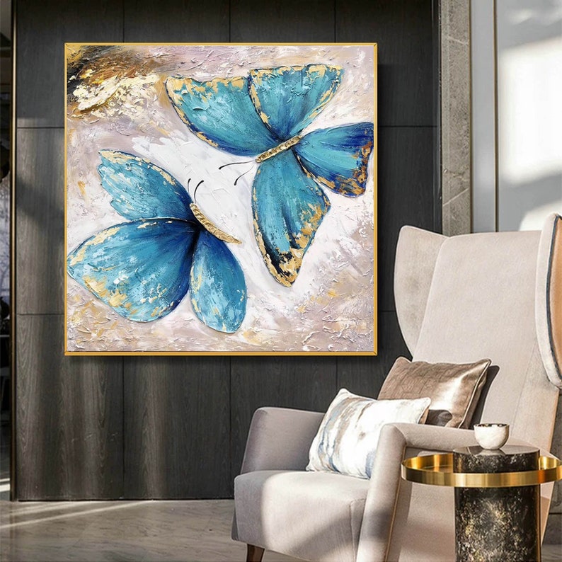 May include: A painting of two blue butterflies with gold accents on a white background. The butterflies are painted in a realistic style and have a textured appearance.
