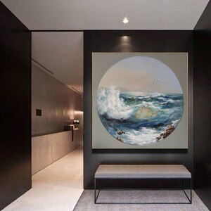 May include: A circular painting of a seascape with a large wave crashing in the foreground. The painting is framed in a black frame and hangs on a wall in a modern hallway.