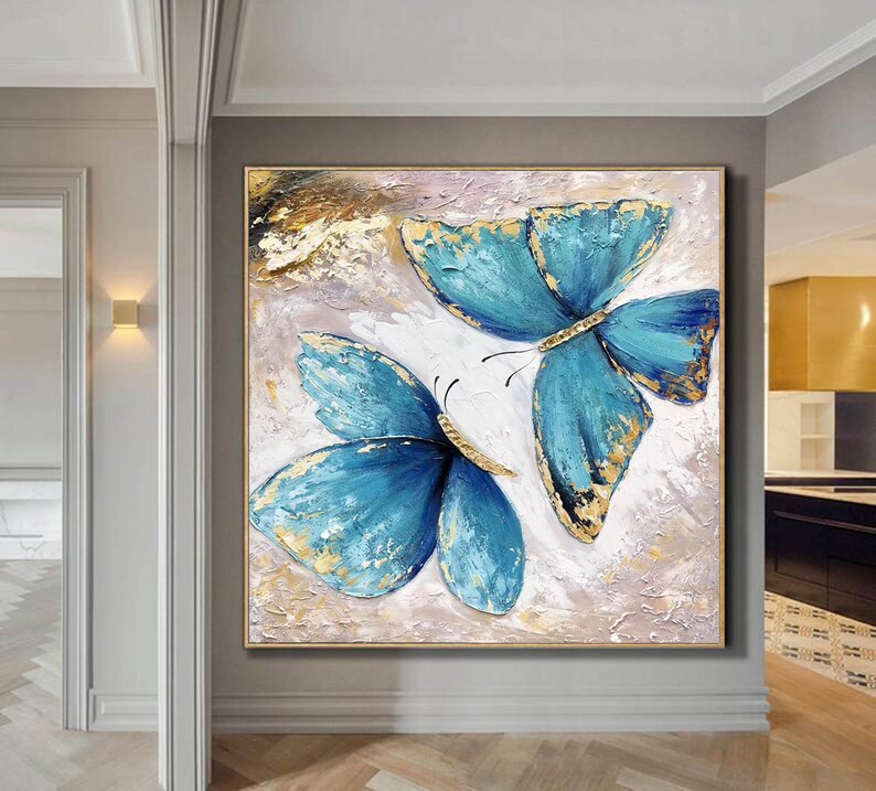 May include: A painting of two blue butterflies with gold accents on a white background. The butterflies are painted in a textured style, giving the painting a three-dimensional effect.
