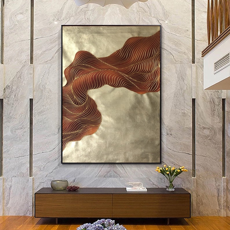 May include: Abstract wall art featuring a gold and brown wave design on a white background. The artwork is framed in a black frame.