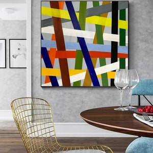 May include: Abstract painting with a geometric design featuring intersecting lines in various colors, including yellow, red, blue, green, white, and brown. The lines are painted on a gray background.