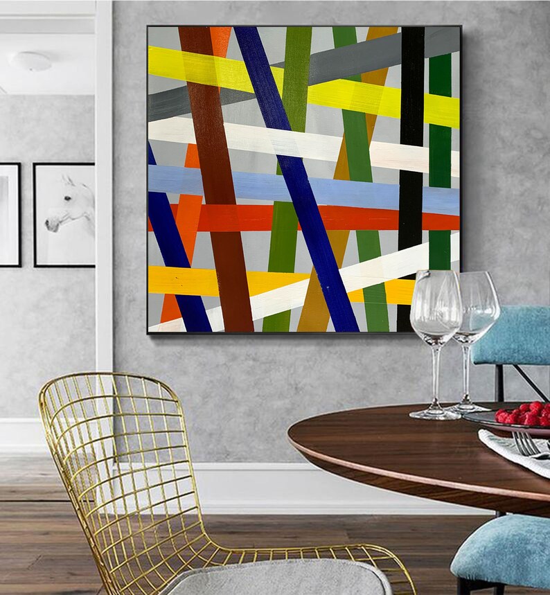 May include: Abstract painting with a geometric design featuring intersecting lines in various colors, including yellow, red, blue, green, white, and brown. The lines are painted on a gray background.