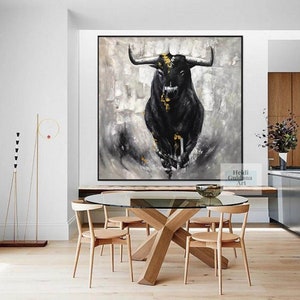 May include: Large framed abstract painting of a black bull with gold accents against a gray and white background. The artwork is displayed in a modern dining room with a glass table and wooden chairs. The artist's name is visible in the bottom right corner.
