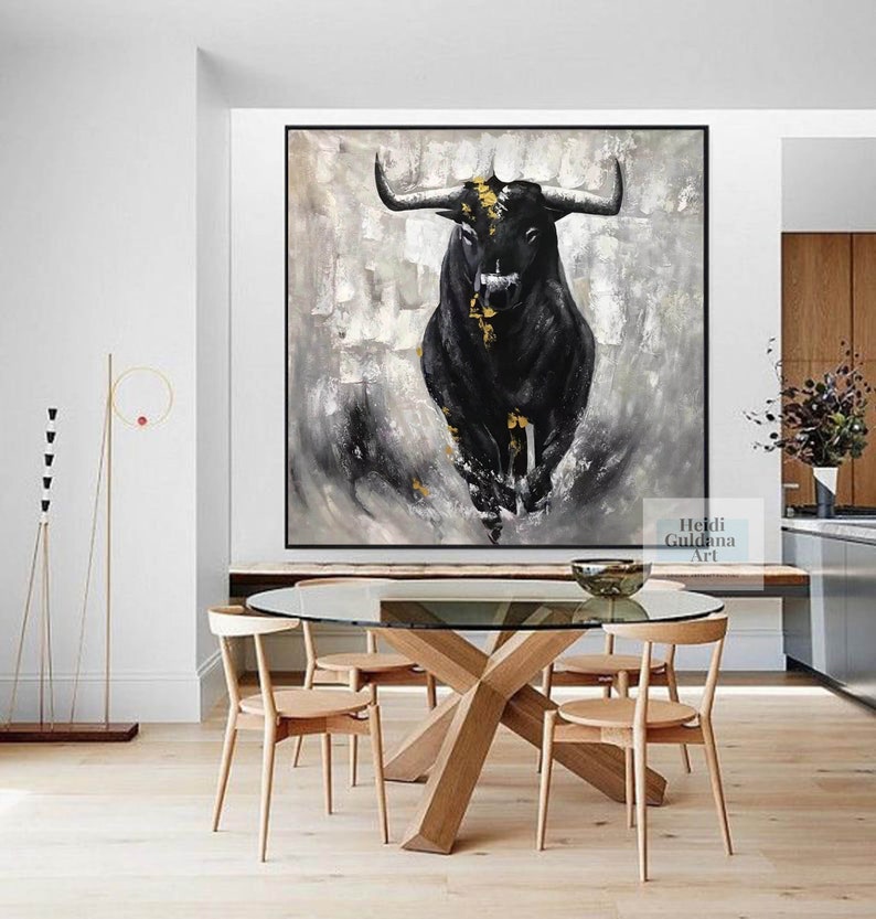 May include: Large framed abstract painting of a black bull with gold accents against a gray and white background. The artwork is displayed in a modern dining room with a glass table and wooden chairs. The artist's name is visible in the bottom right corner.