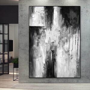 Puede incluir: Pintura abstracta en blanco y negro con pinceladas gruesas y goteos de pintura. La pintura est&aacute; enmarcada y colgada en una pared.