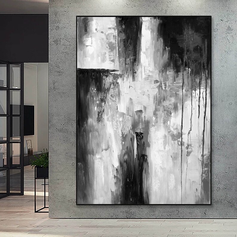 Puede incluir: Pintura abstracta en blanco y negro con pinceladas gruesas y goteos de pintura. La pintura est&aacute; enmarcada y colgada en una pared.
