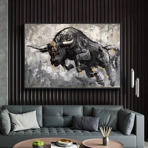 May include: A black and gold abstract painting of a bull charging forward. The bull is painted in a bold, expressive style with thick brushstrokes. The background is a muted gray with hints of gold.