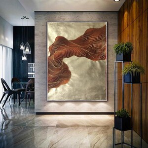May include: Abstract wall art featuring a gold and brown wave design. The artwork is framed and hanging on a wall in a modern home.