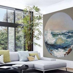 May include: A circular painting of a seascape with crashing waves and a blue sky with white clouds. The painting is framed in a light gray frame and is hanging on a wall in a living room.