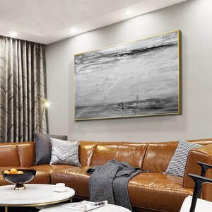 Op de afbeelding: Een groot abstract schilderij in grijstinten en zwart hangt aan een muur boven een bruine leren bank. Het schilderij heeft een horizontale ori&euml;ntatie en heeft een textuur met penseelstreken.
