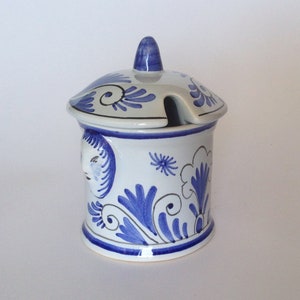 Puede incluir: Un azucarero de cerámica blanca con un diseño floral azul y blanco. La tapa tiene un pequeño pico para verter y un diseño floral azul y blanco.