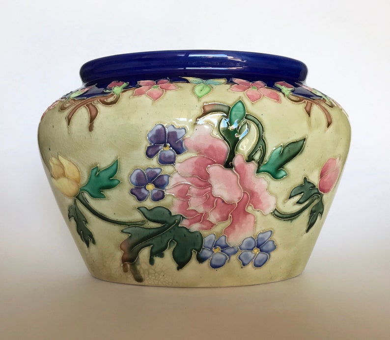 May include: A cream-colored ceramic planter with a blue rim and a floral design. The flowers are pink, yellow, blue, and green.