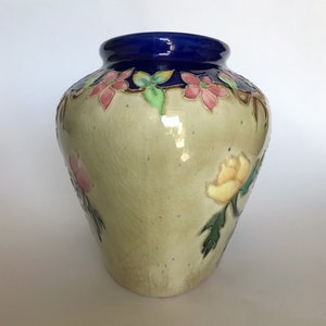 May include: A ceramic vase with a blue rim and floral designs in shades of pink, yellow, and green. The vase has a crackled glaze and a light beige background.