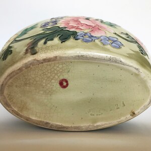 May include: A green ceramic vase with a floral design featuring pink, purple, and green flowers. The vase has a crackled glaze and a red dot on the bottom. The bottom of the vase is marked "Gottleib  21  Germany".