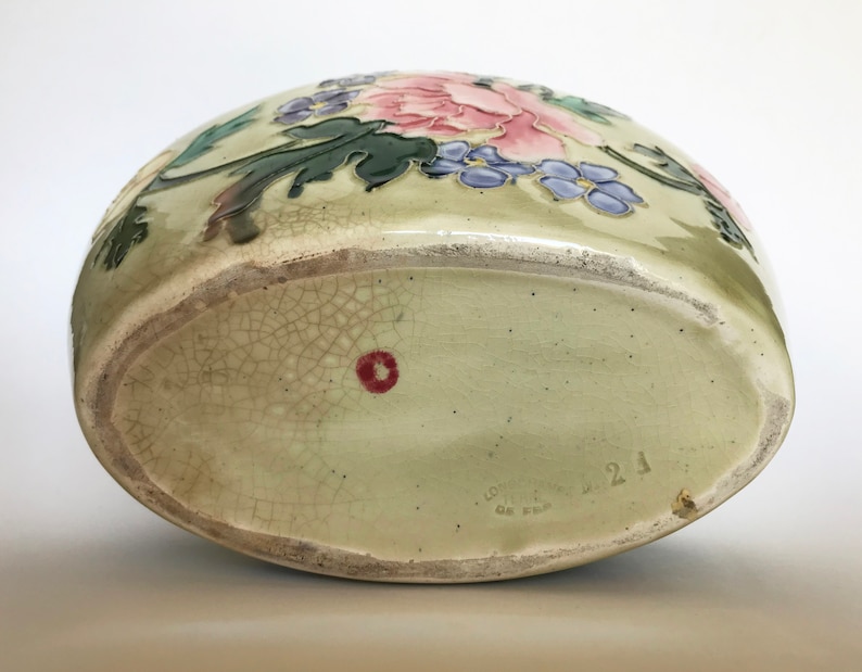 May include: A green ceramic vase with a floral design featuring pink, purple, and green flowers. The vase has a crackled glaze and a red dot on the bottom. The bottom of the vase is marked "Gottleib  21  Germany".