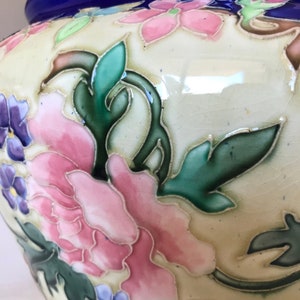 May include: A white ceramic planter with a blue rim and floral design. The planter features pink, blue, and green flowers with intricate details.