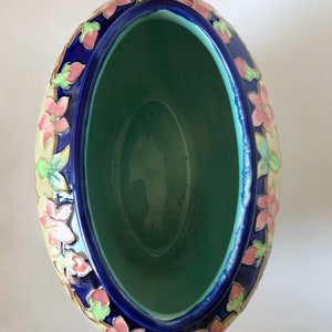 May include: An oval ceramic planter with a blue glaze and floral design. The planter has a light green interior and is decorated with pink, yellow, and green flowers.