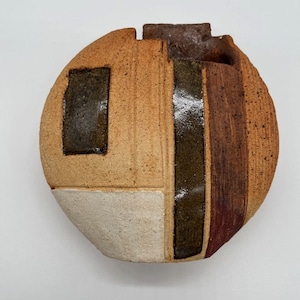 May include: A round ceramic vase with a geometric design in shades of brown, white, and green. The vase has a textured surface and a small opening at the top.