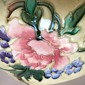 May include: Close-up of a ceramic bowl with a floral design. The bowl is decorated with pink, purple, and blue flowers and green leaves. The background is a light cream color.