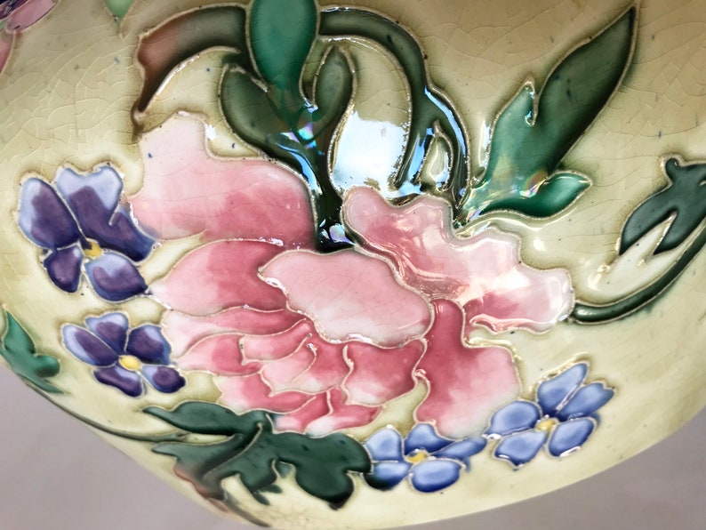 May include: Close-up of a ceramic bowl with a floral design. The bowl is decorated with pink, purple, and blue flowers and green leaves. The background is a light cream color.