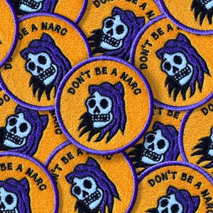 May include: Embroidered patches with a skull wearing a purple hood and the text "DON'T BE A NARC" in white. The patches are round with a yellow background and purple border. The patches are scattered.