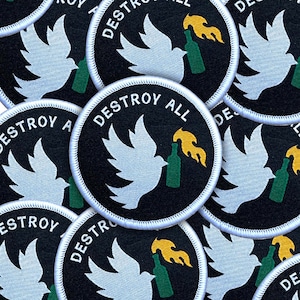 May include: Circular black patches with white stitching feature a white dove holding a green bottle with a yellow flame. The text "DESTROY ALL" is in white, arched around the top of the patch.