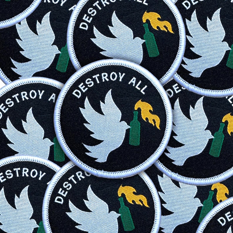 May include: Circular black patches with white stitching feature a white dove holding a green bottle with a yellow flame. The text "DESTROY ALL" is in white, arched around the top of the patch.
