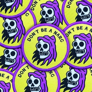 May include: A collection of round patches with a yellow background and a purple border. Each patch features a skull with purple hair and the text "DON'T BE A NARC" in black. The patches are scattered across the image.