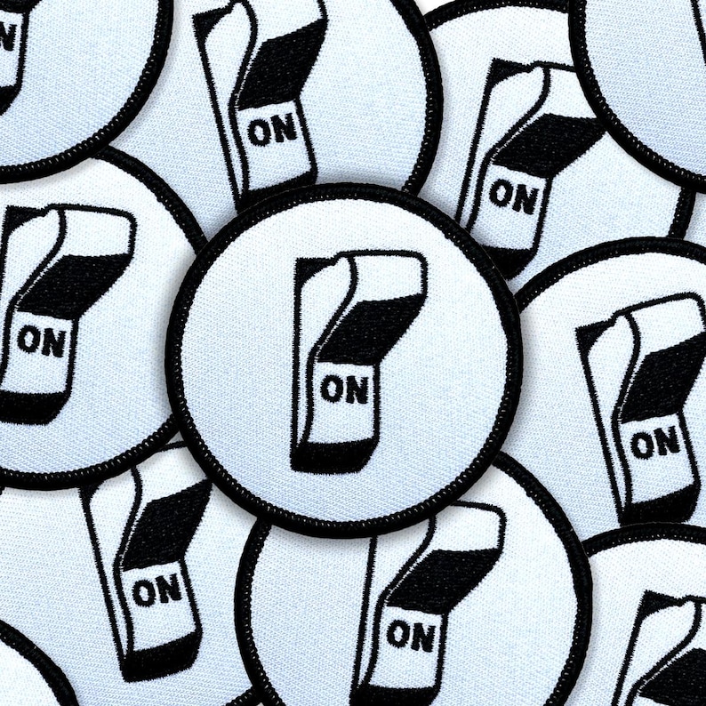 May include: Circular white patches with a black border, each featuring a black and white graphic of a switch in the 'ON' position. The word 'ON' is printed in black on the switch. The patches are made of a textured fabric.