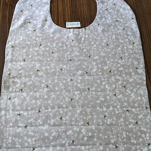 May include: A large, quilted bib with a pink background and a white floral pattern with small black bees. The bib has a velcro closure at the neck and says "LARGE" on the front.