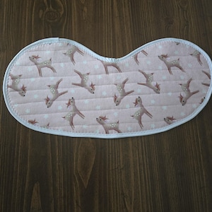 May include: A baby bib with a pink background featuring a pattern of deer and white stars. The bib has a quilted texture and a white trim. The bib is designed to catch spills and drool.
