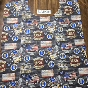 May include: A large, gray bib with a patriotic design featuring eagles, American flags, and the text "Respect Freedom" and "USA Air Force." The bib has a curved neckline and a rectangular body.