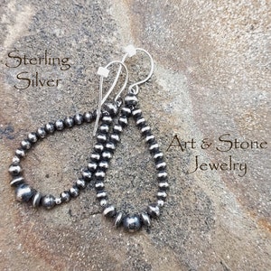 May include: Sterling silver teardrop earrings. Each earring features a series of small, round, silver beads, creating a textured, beaded appearance. The earrings are suspended from silver hooks. The text "Art & Stone Jewelry" is visible.
