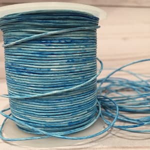 May include: A spool of light blue leather cord with a white marbled pattern. The cord is wound around a white plastic spool.