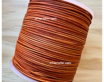 May include: A spool of orange-brown leather cord, wound tightly. The cord is smooth and appears to be supple. The label on the spool reads "antique leather supply".