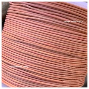 Puede incluir: Primer plano de un carrete de cordón de cuero rosa claro. El cordón está enrollado apretado y tiene una superficie lisa ligeramente texturizada. El texto "antique leather supply" es visible en el carrete.