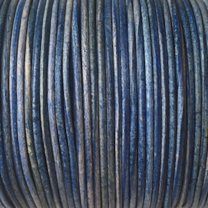 May include: Close-up of a spool of blue and white leather cord. The cord is tightly wound and has a textured surface.