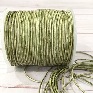 May include: A spool of green leather cord. The cord is wound tightly around the spool and is ready to be used for crafting projects.