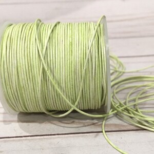 May include: A spool of light green leather cord. The cord is wound tightly around the spool and is ready to be used for crafting projects.