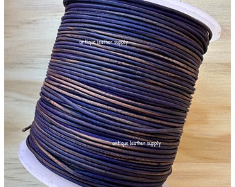 May include: A spool of dark blue leather cord with a copper-toned sheen. The cord is wound tightly around a white plastic spool. The text "antique leather supply" is printed on the spool.