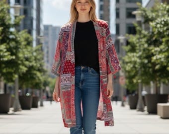 May include: A long, open-front kimono featuring a vibrant red, blue, and white patchwork pattern with intricate floral and geometric motifs. The garment is worn over a plain black t-shirt, blue denim jeans, and white sneakers in an urban setting.